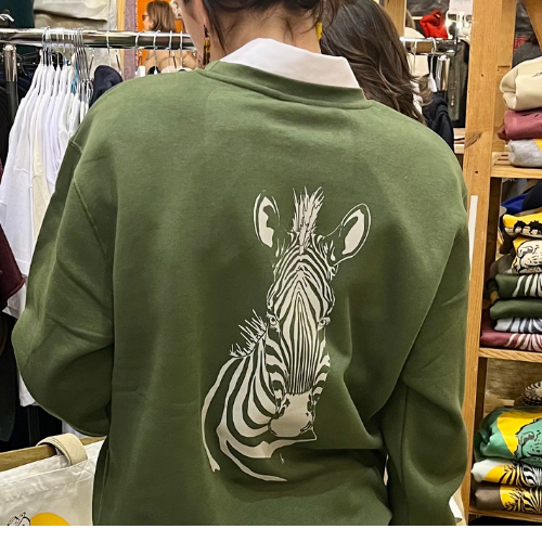 Chica de espaldas en un m,ercadillo. Lleva una sudadera sin capucha de color verde aventura y un diseño de una cebra en color beige